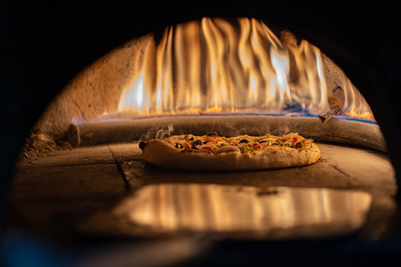 A delicious pizza baking in a traditional wood-fired oven with vibrant flames.